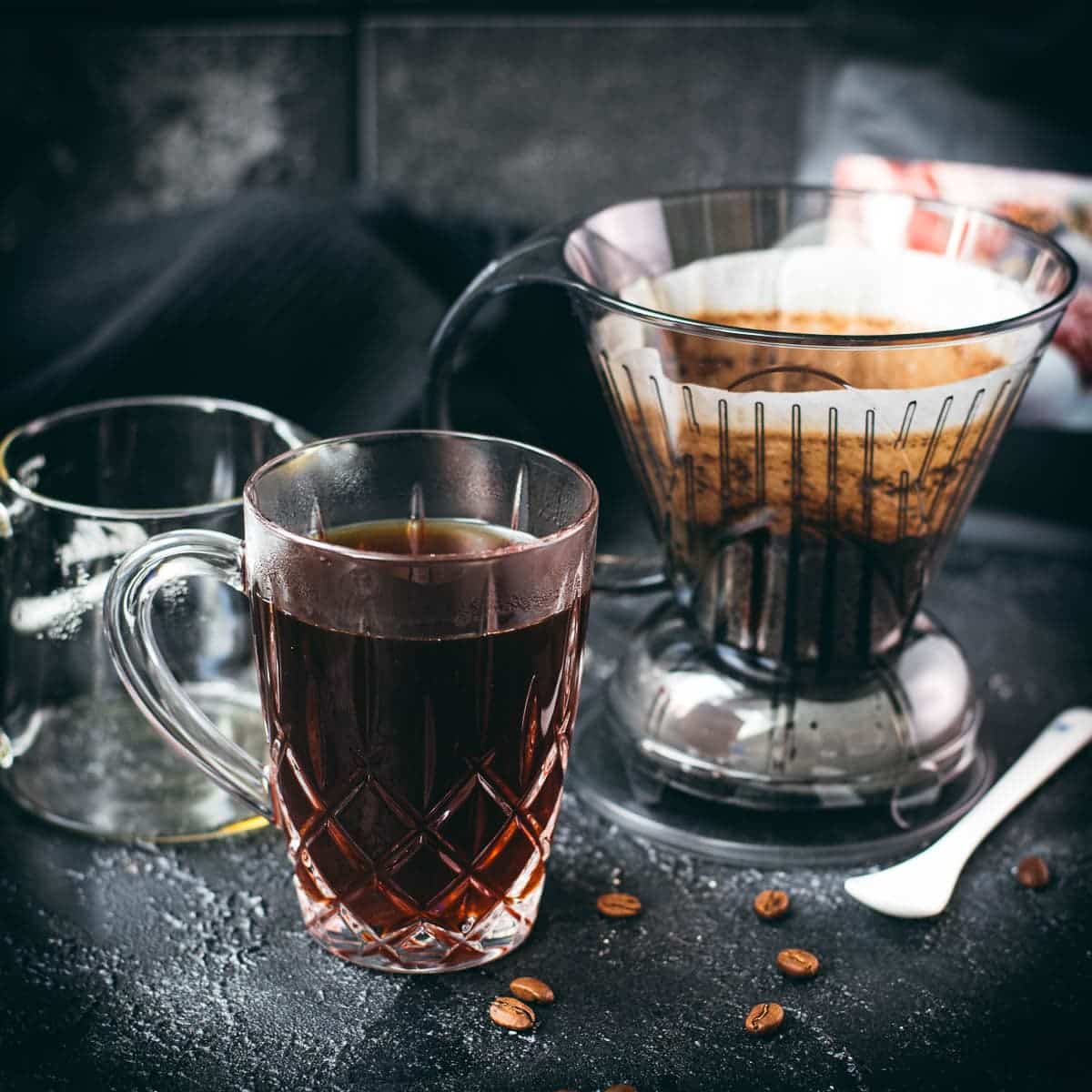 Used Clever Dripper with wet coffee grounds beside a glass mug of freshly brewed coffee.