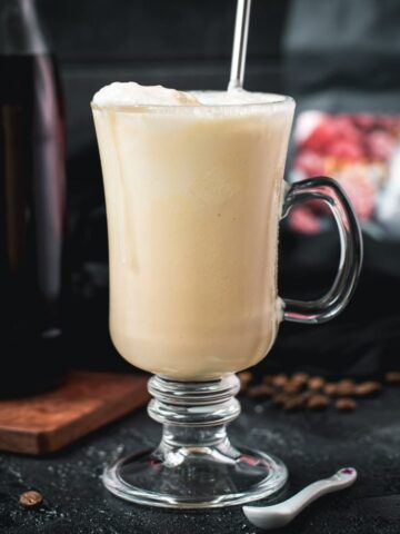 Serving glass filled with homemade coffee milkshake, topped with cold frothed milk and served with a reusable drinking straw.