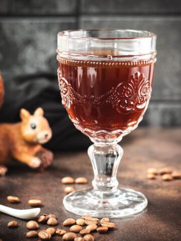 Gorgeous glass filled with maple syrup coffee, placed on dark brown ground, next to squirrel figure.